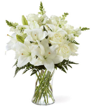 A bouquet of white lilies, roses, and snapdragons, with fresh floral greens, in a tall clear cylinder vase ready for Illinois delivery