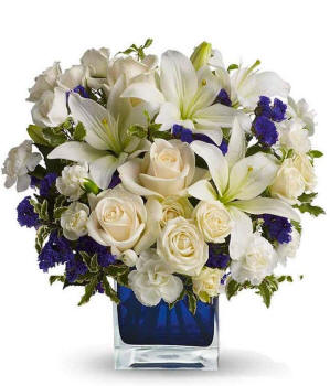 Arizona Floral arrangement featuring cr&egrave;me roses, cr&egrave;me spray roses, white Asiatic lilies, white miniature carnations, and purple statice in a blue cube vase.